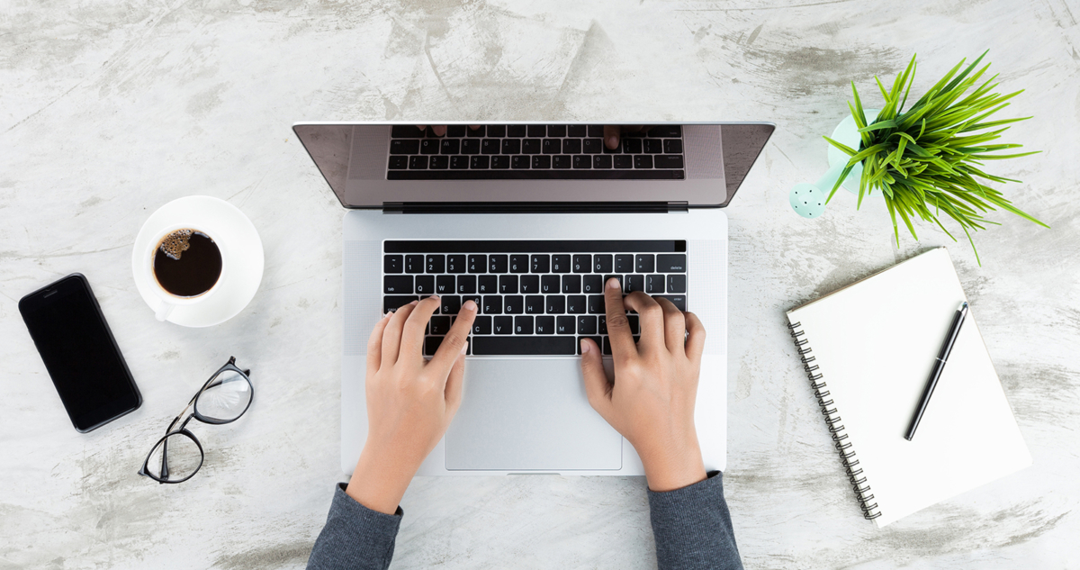 Laptop on desk with paper pad, coffee cup, glasses, and phone